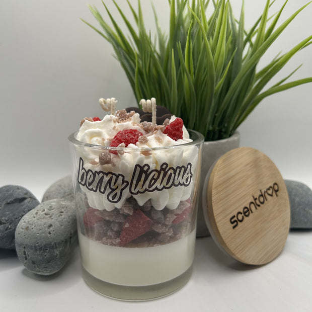 Glass jar with dessert and whipped cream labeled 'Berrylicious' next to a wooden lid with 'scentdrop' branding.