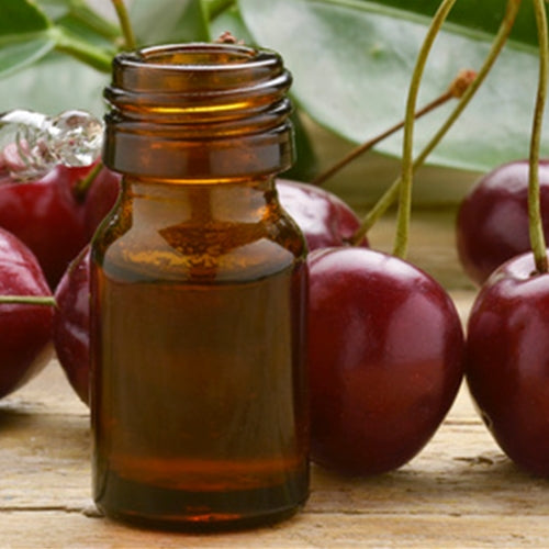 Amber glass bottle with cherry juice surrounded by cherries on a wooden surface