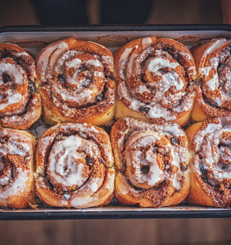 Baked cinnamon rolls with icing in a baking tray