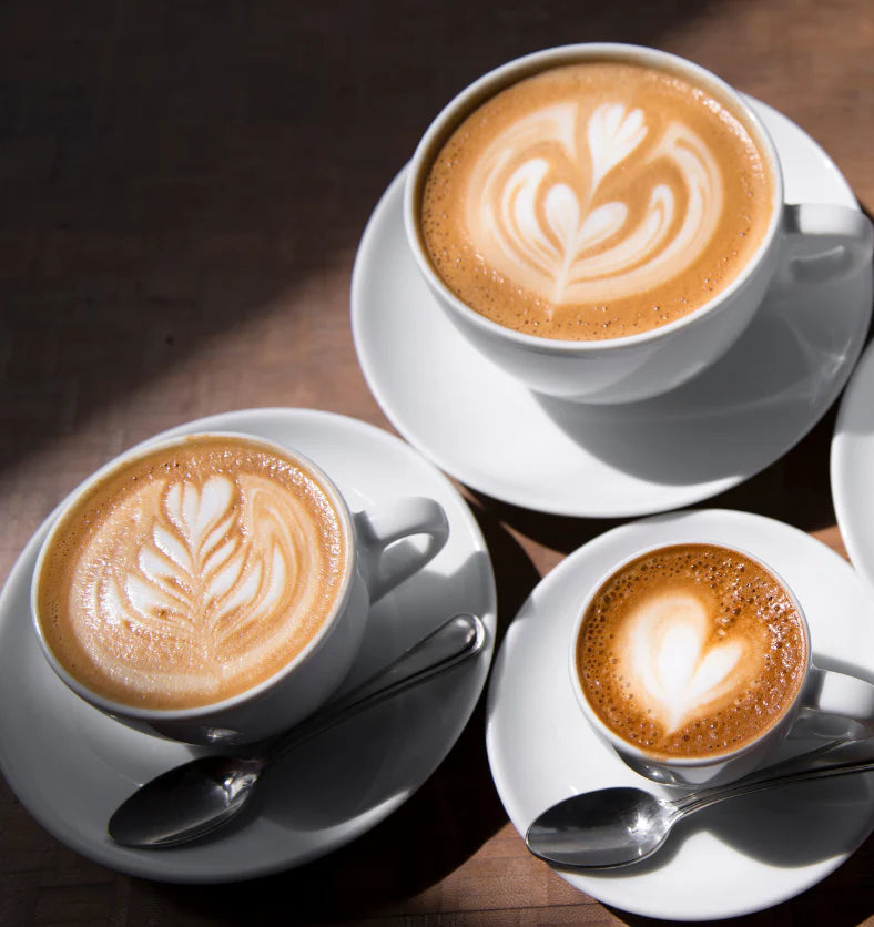 Three cups of cappuccino with latte art on a wooden table.