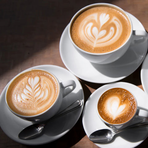 Three cups of cappuccino with latte art on a wooden table.