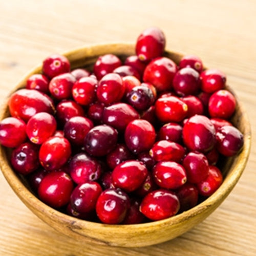 Wooden bowl filled with red cranberries on a wooden surface