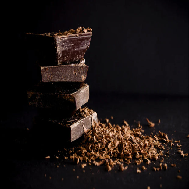 Stack of dark chocolate bars with some broken pieces on a dark background