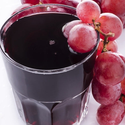 Glass of red grape juice with a bunch of red grapes on a white background