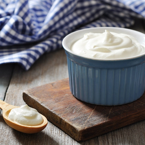 Blue bowl of whipped cream on a wooden board with a checkered cloth in the background