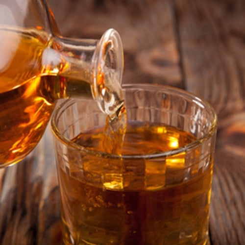 Glass being filled with amber liquid from a decanter on a wooden surface.