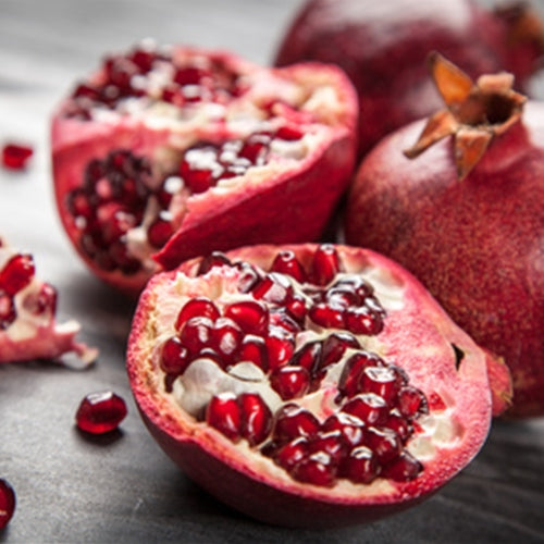 Pomegranate with a few pieces cut open on a dark surface