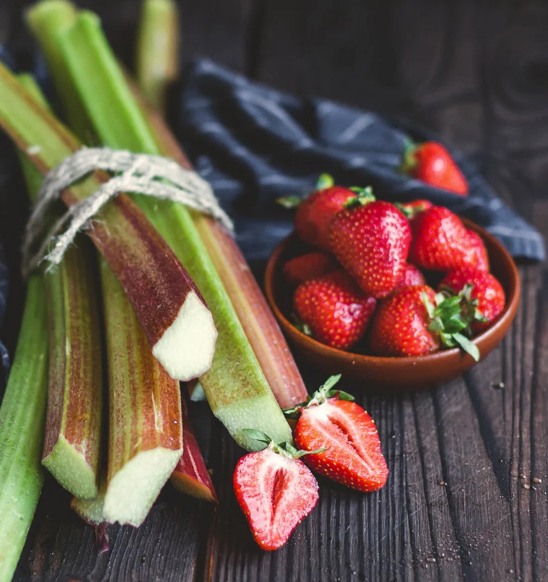 Rhubarb and strawberries on a dark wood table top.
