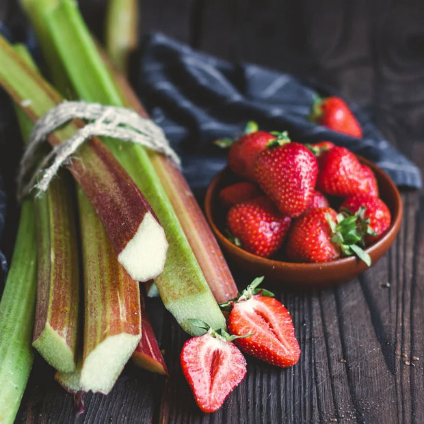 Rhubarb and strawberries on a dark wood table top.