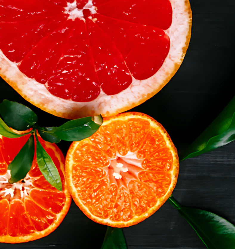 Sliced grapefruit and oranges on a dark surface with green leaves.