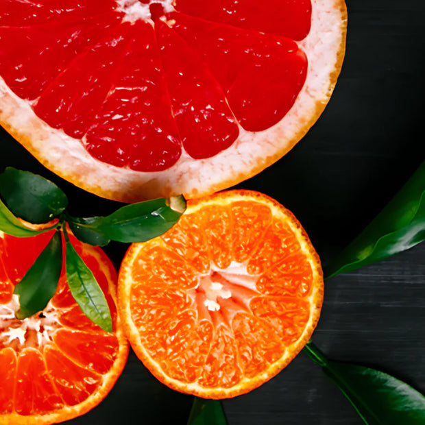 Sliced grapefruit and oranges on a dark surface with green leaves.