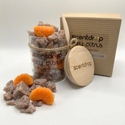 A scented bath soak product set on a white studio background, featuring a clear jar filled with chunky beige crystals and bright orange citrus slices, a round wooden lid engraved with the brand name, and a kraft paper box labeled 'scentdrop berry citrus'.