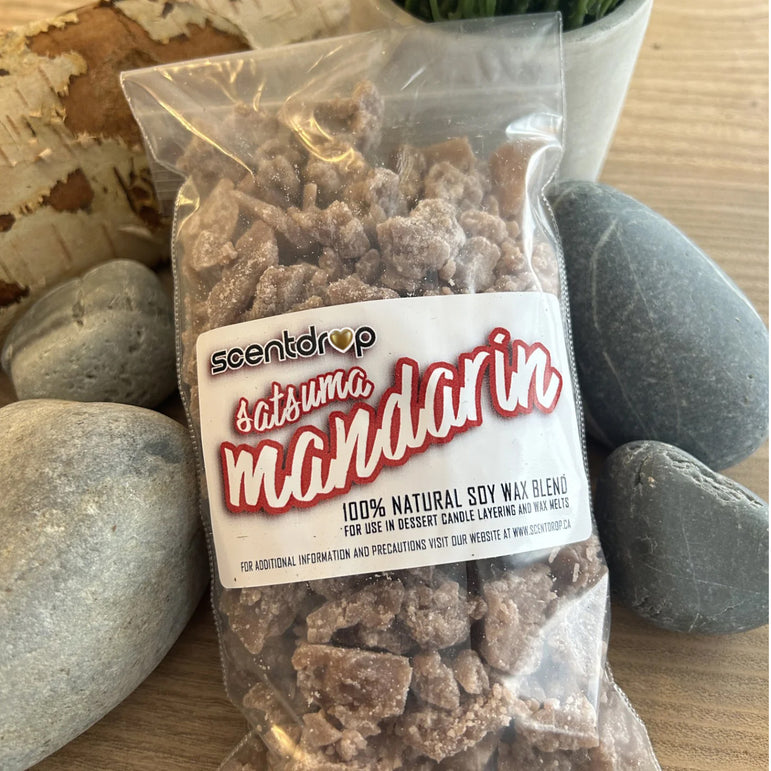 A clear plastic bag of Scentdrop Satuma Mandarin soy wax blend wax melts, displayed on a wooden surface with decorative gray stones.