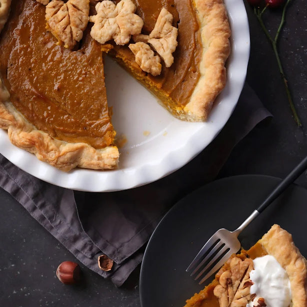 A spiced pumpkin pie cut with a piece on a plate on a black dark background