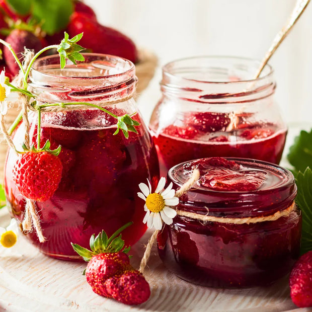 Three jars of strawberry jam with fresh strawberries on a wooden surface