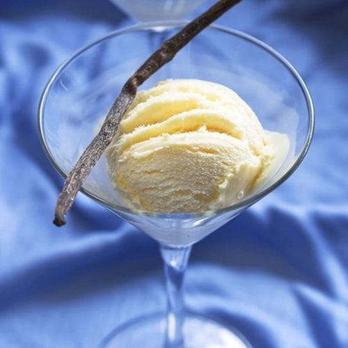 Vanilla ice cream in a martini glass with a vanilla bean on a blue background