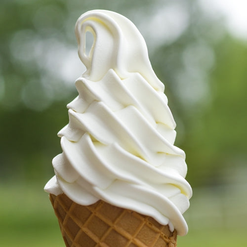 Ice cream cone with white soft serve ice cream against a blurred green background