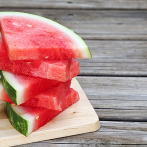 Sliced watermelon on a wooden cutting board with a wooden background