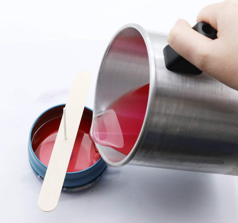 Hand pouring red liquid from a metal container with a white stick into another container.
